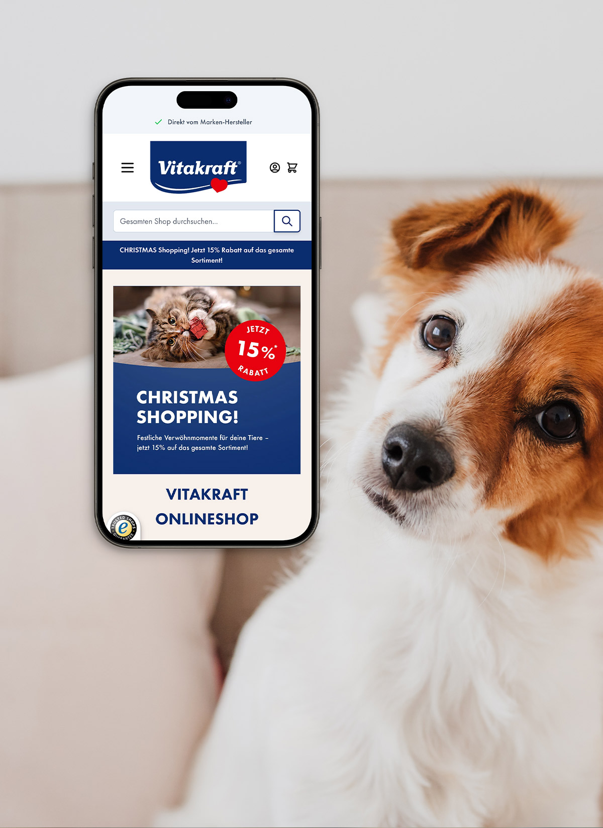 Smartphone mit Vitakraft Shop offen und einem Hund daneben